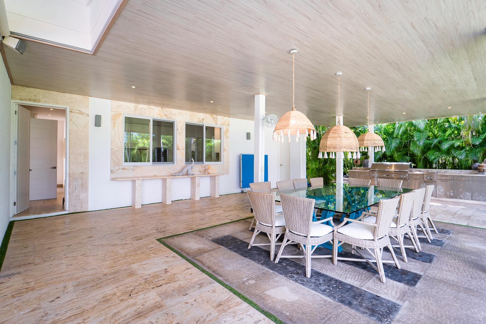 Covered patio with wicker dining chairs, woven pendant lights, and a stainless-steel outdoor kitchen.