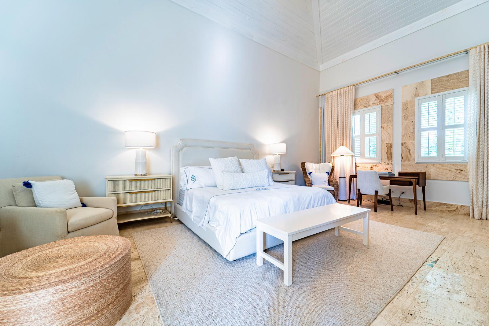 Bright bedroom with a vaulted ceiling, shuttered windows, and a sitting area.