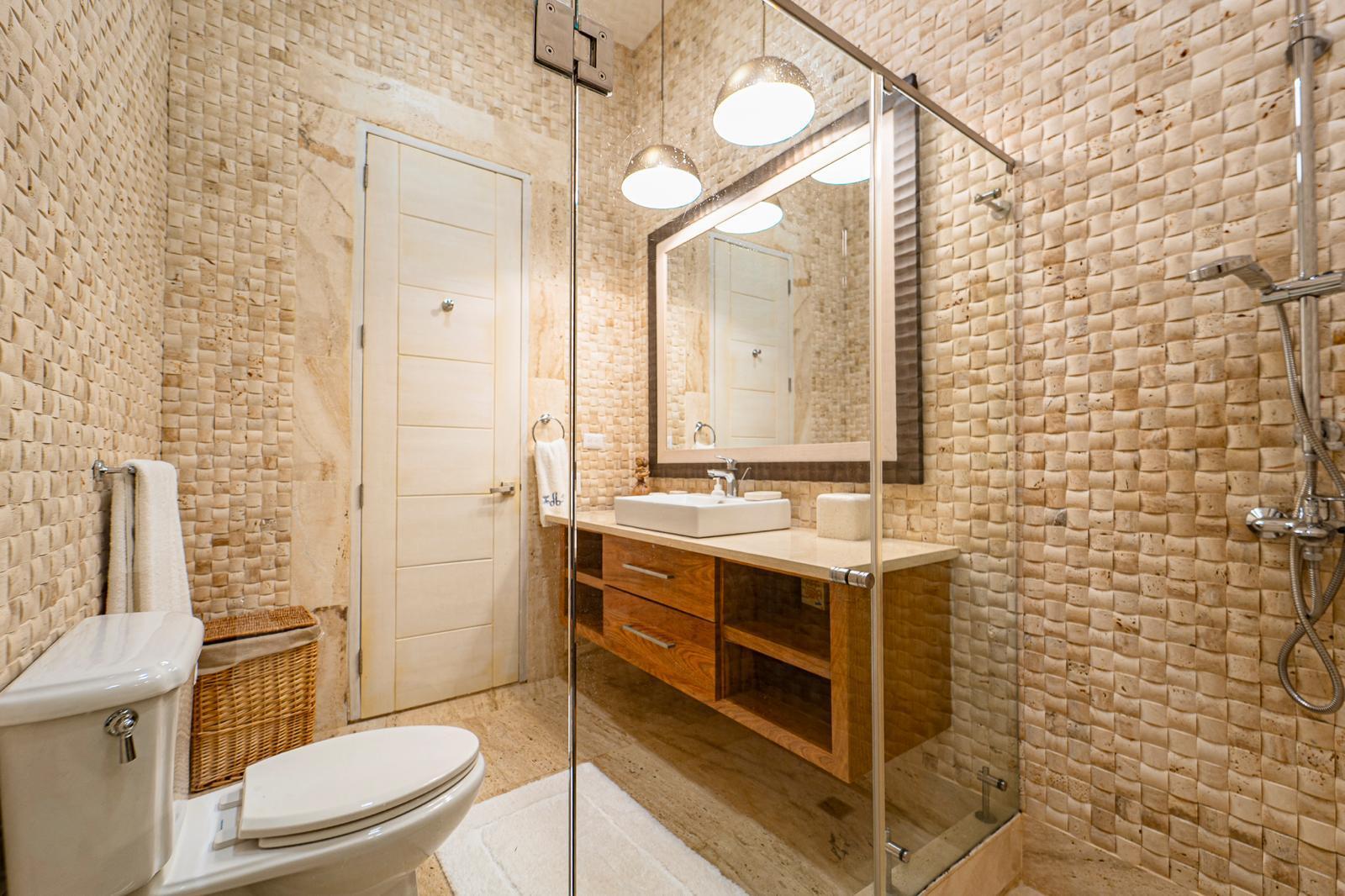 Bathroom with textured beige tile, glass shower enclosure, and wood vanity.