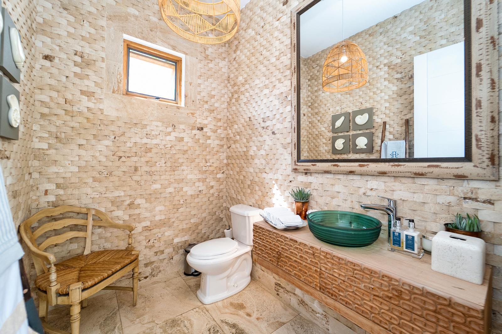 Bathroom with a green vessel sink on a carved vanity, stone walls, and a wooden chair.