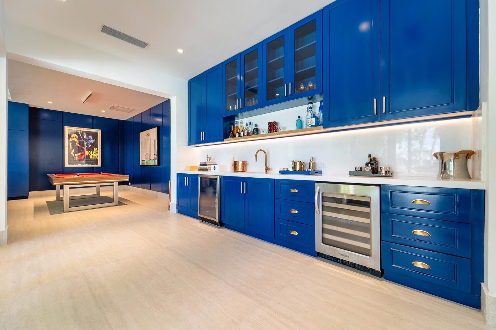 Kitchen with vivid blue cabinetry, wine refrigerator, and adjoining billiard room.