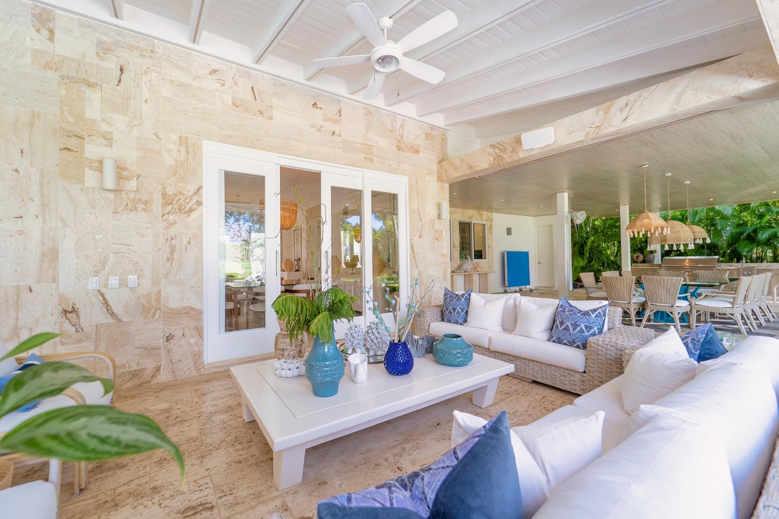 Covered patio with wicker lounge seating, a dining area, and lush tropical greenery.