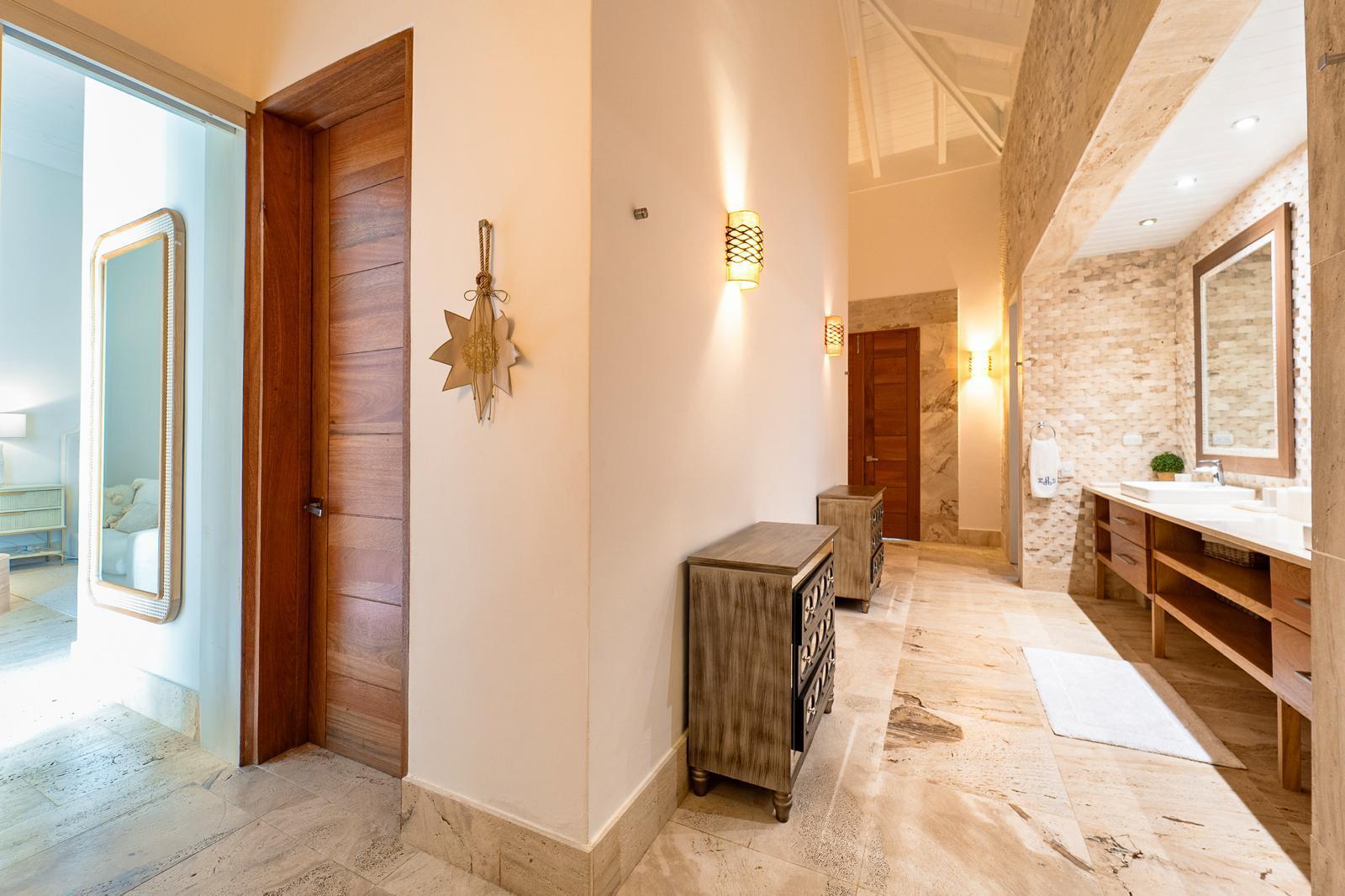 Bathroom with a long double vanity, stone finishes, and an open doorway to a bedroom.