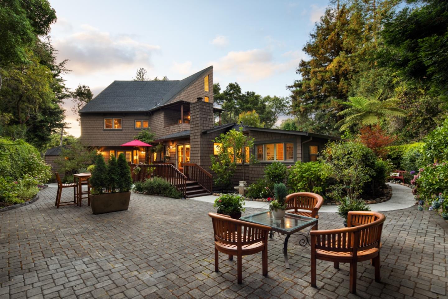 Shingle-clad home with a spacious paved patio, wooden dining furniture, and lush garden landscaping.