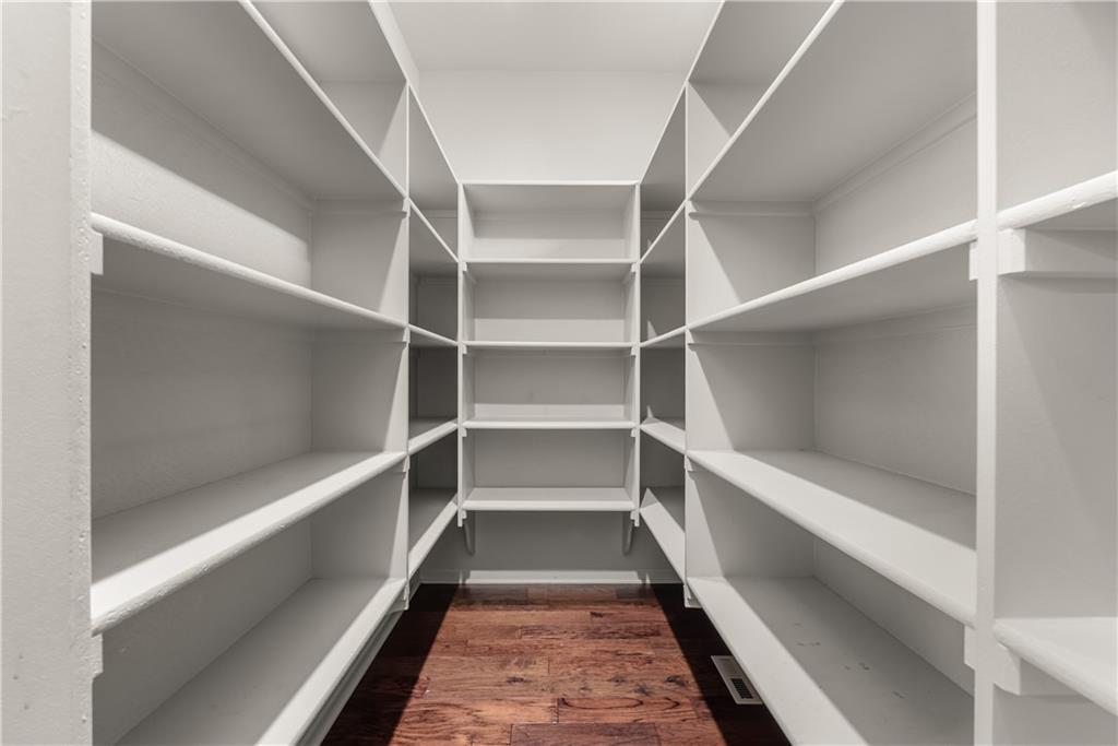 Walk-in storage room with white built-in shelves and a dark wood floor.