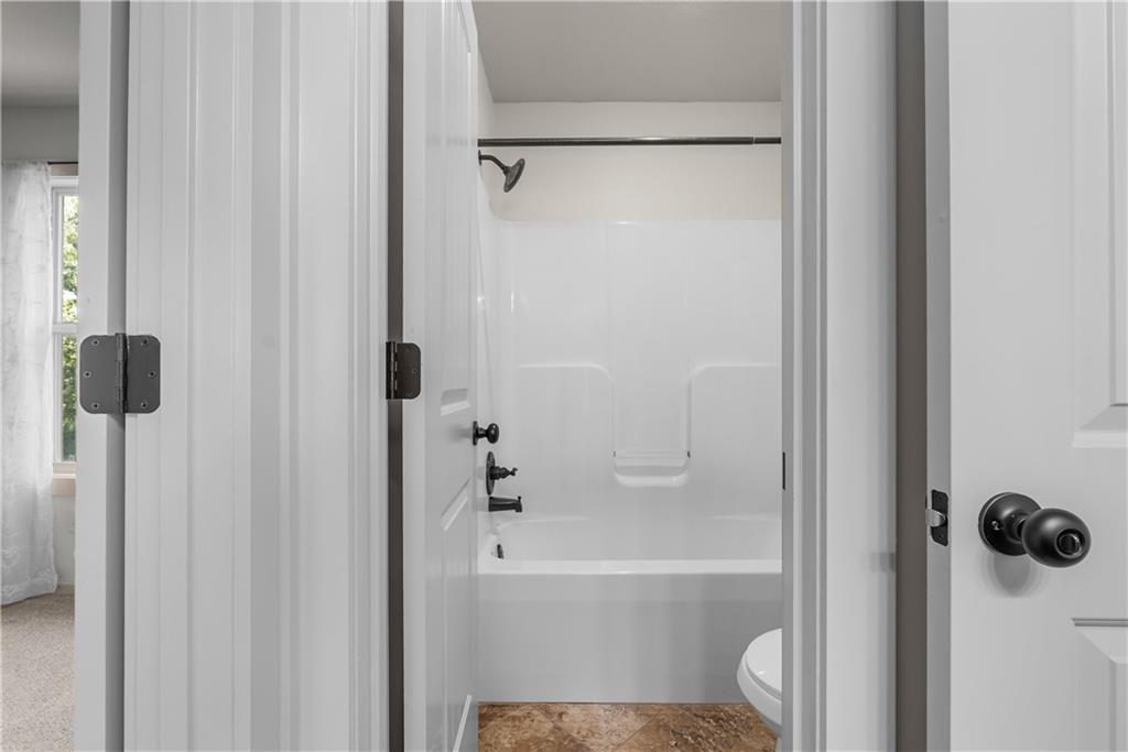 Bathroom with a white bathtub and shower surround, dark fixtures, and brown flooring.