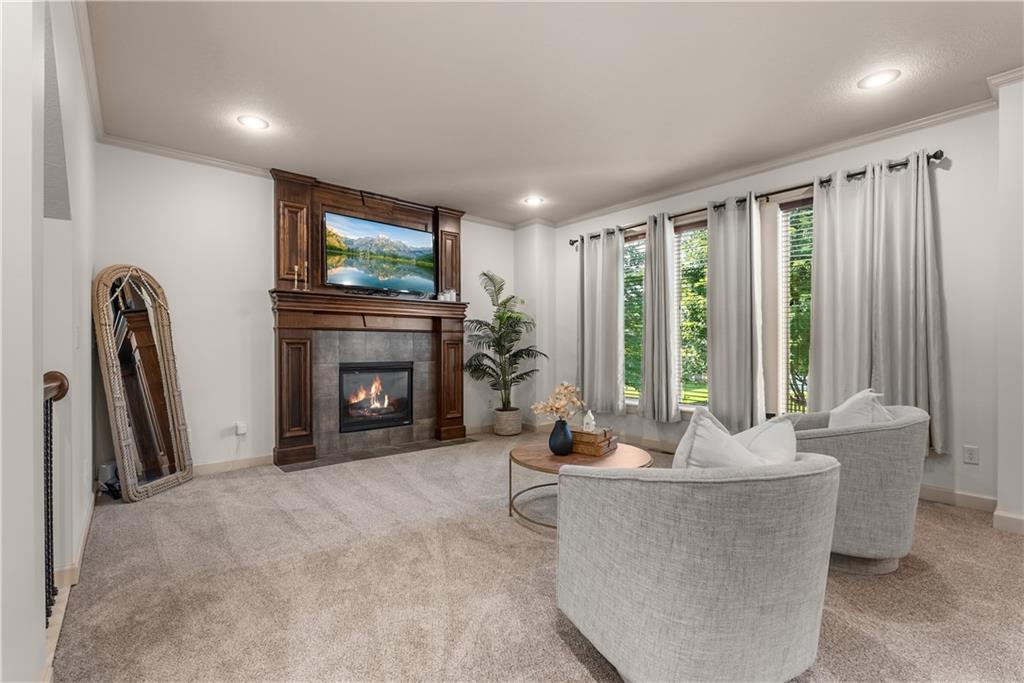 Staged living room with a stone fireplace, dark wood mantel, and tall curtained windows.