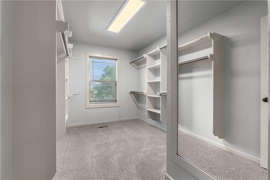 Walk-in closet with built-in shelving, hanging rods, and a window with blinds.