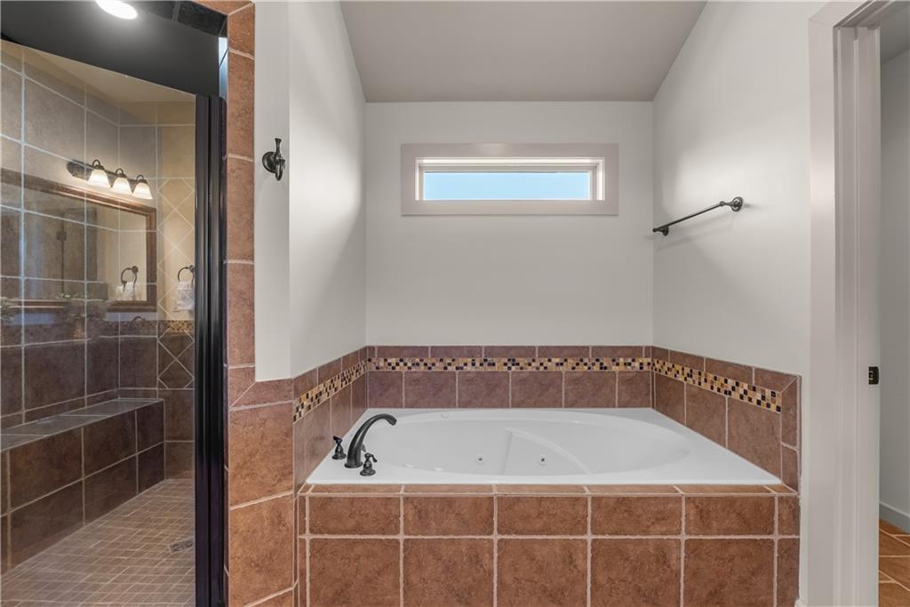 Bathroom with a tiled soaking tub beside a glass-enclosed shower and narrow high window.