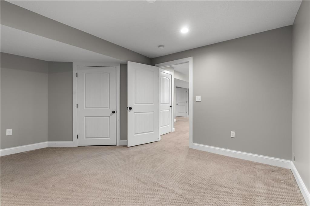 Empty carpeted room with gray walls and open white doors leading to a hallway.