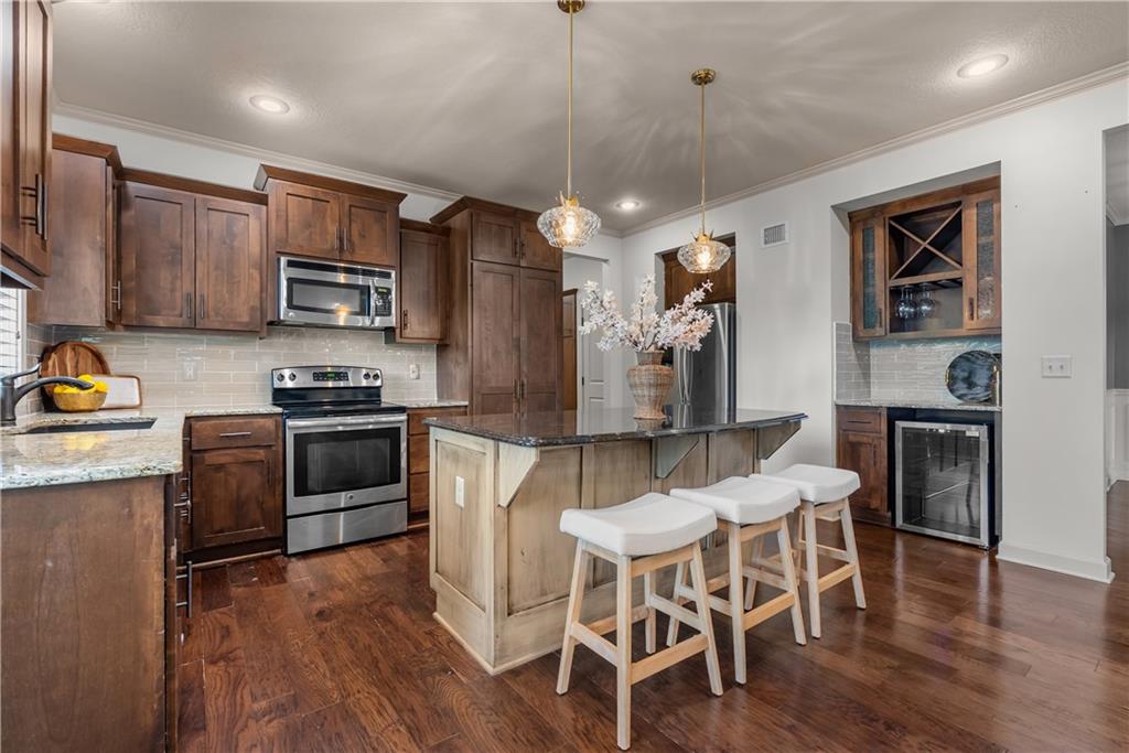 Kitchen with dark wood cabinets, stainless steel appliances, and an island with three white stools.