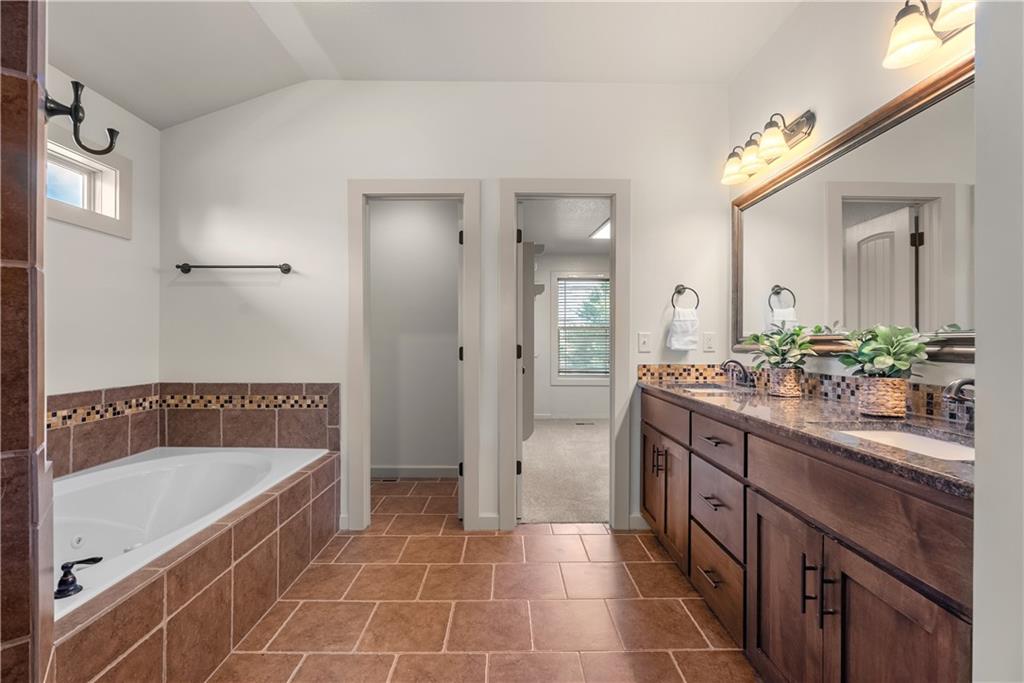 Bathroom with a tiled corner soaking tub and long wooden double vanity beneath a large mirror.