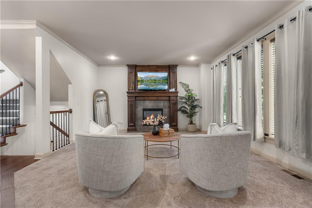 Living room with curved sofas, a dark wood fireplace, tall curtained windows, and a staircase.