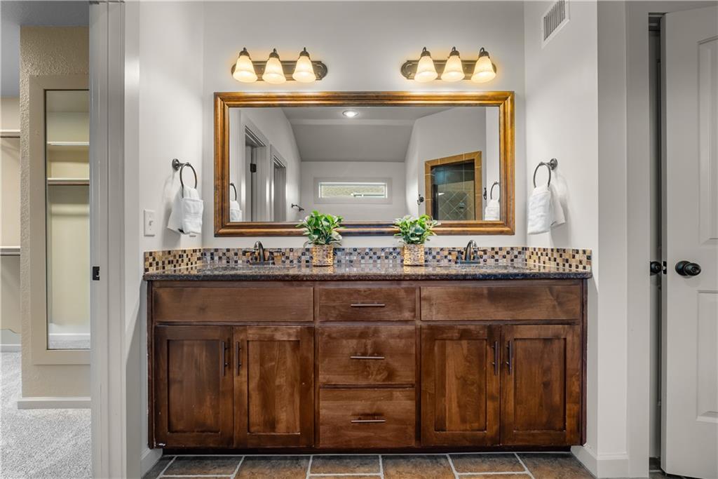 Bathroom with a wide dark wood double vanity, mosaic backsplash, and large framed mirror.