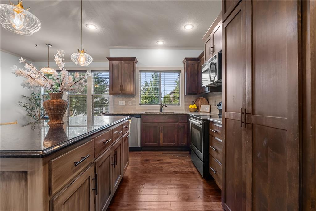 Kitchen with dark wood cabinetry, granite counters, stainless appliances, and hardwood floors.