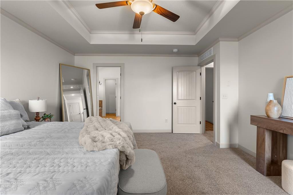 Bedroom with white bedding, a tray ceiling, and a ceiling fan.