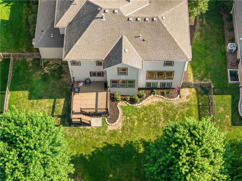 Rear of a two-story house with a raised deck, landscaped garden beds, and a tree-lined backyard.