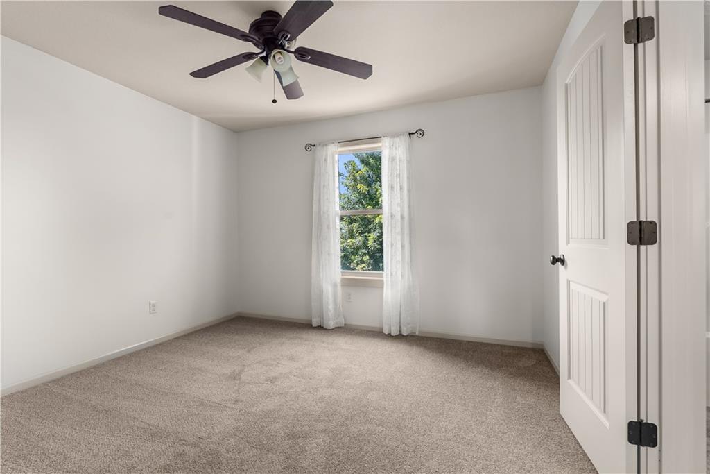 Empty bedroom with beige carpet, sheer window curtains, and a dark ceiling fan.