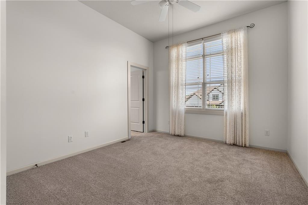 Empty bedroom with beige carpet, a ceiling fan, and a curtained window with blinds.
