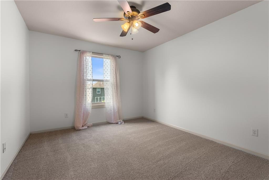 Empty bedroom with beige carpet, a ceiling fan, and sheer pink curtains framing the window.