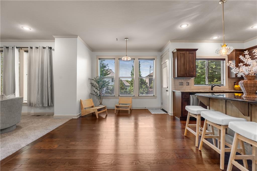 Open-plan kitchen with a dark wood island, white stools, hardwood floors, and a sitting area by the windows.
