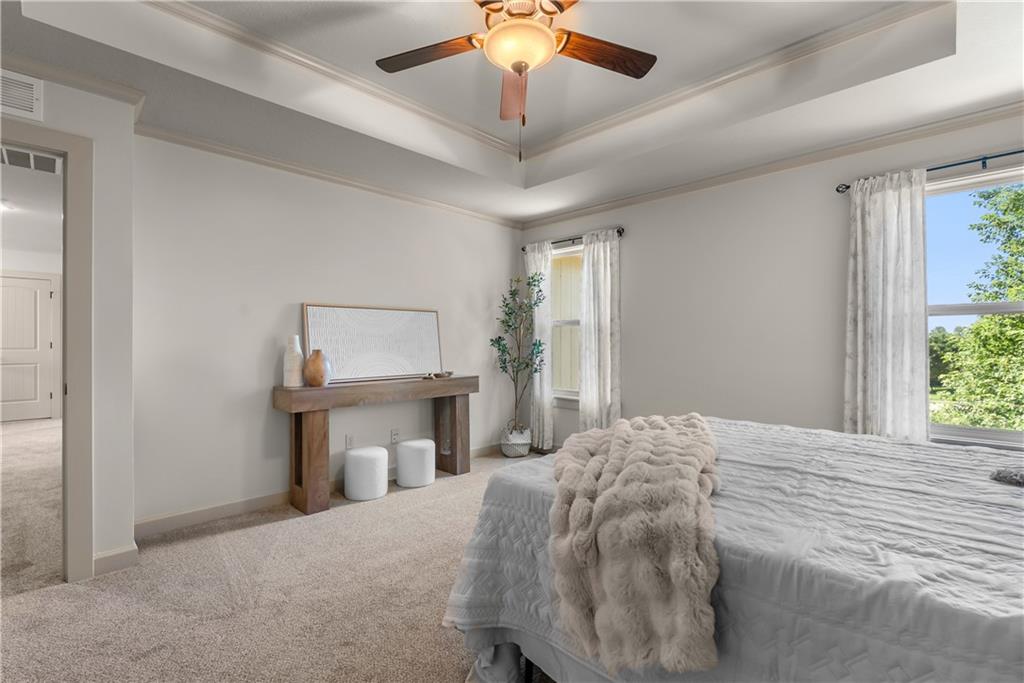 Bedroom with a tray ceiling, ceiling fan, white bedding, and windows overlooking trees.