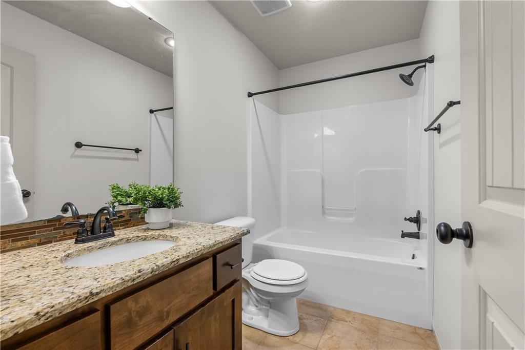 Bathroom with a granite vanity, wooden cabinet, and white tub-shower.
