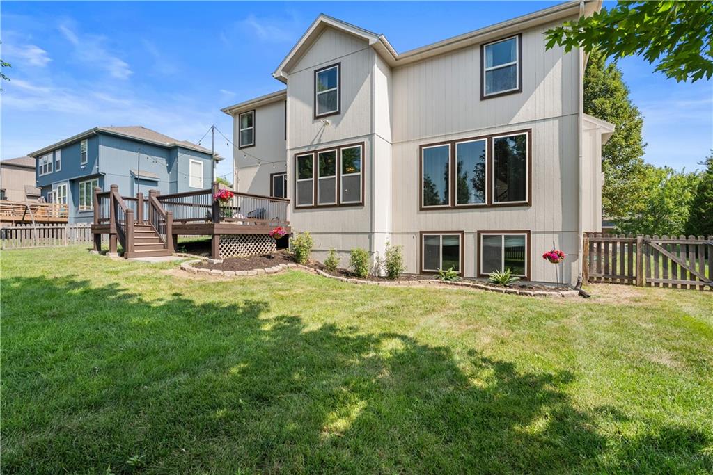 Two-story home with a raised deck, broad windows, and a fenced grassy backyard.