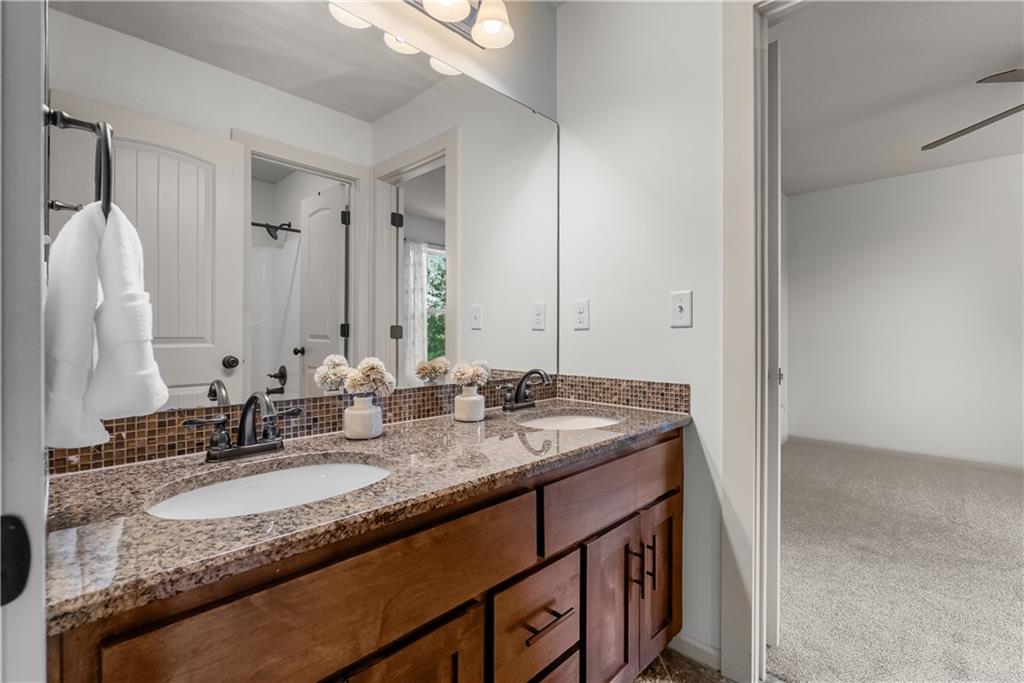 Bathroom with a double-sink granite vanity and dark wood cabinetry beside an adjoining carpeted room.