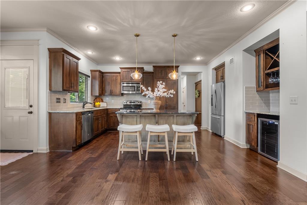 Kitchen with a large island, three stools, dark wood cabinets, and stainless steel appliances.