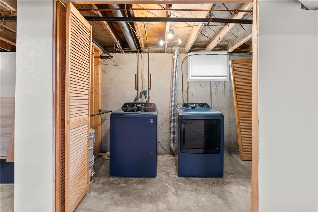 Basement laundry room with a blue washer and dryer beneath exposed ceiling joists.