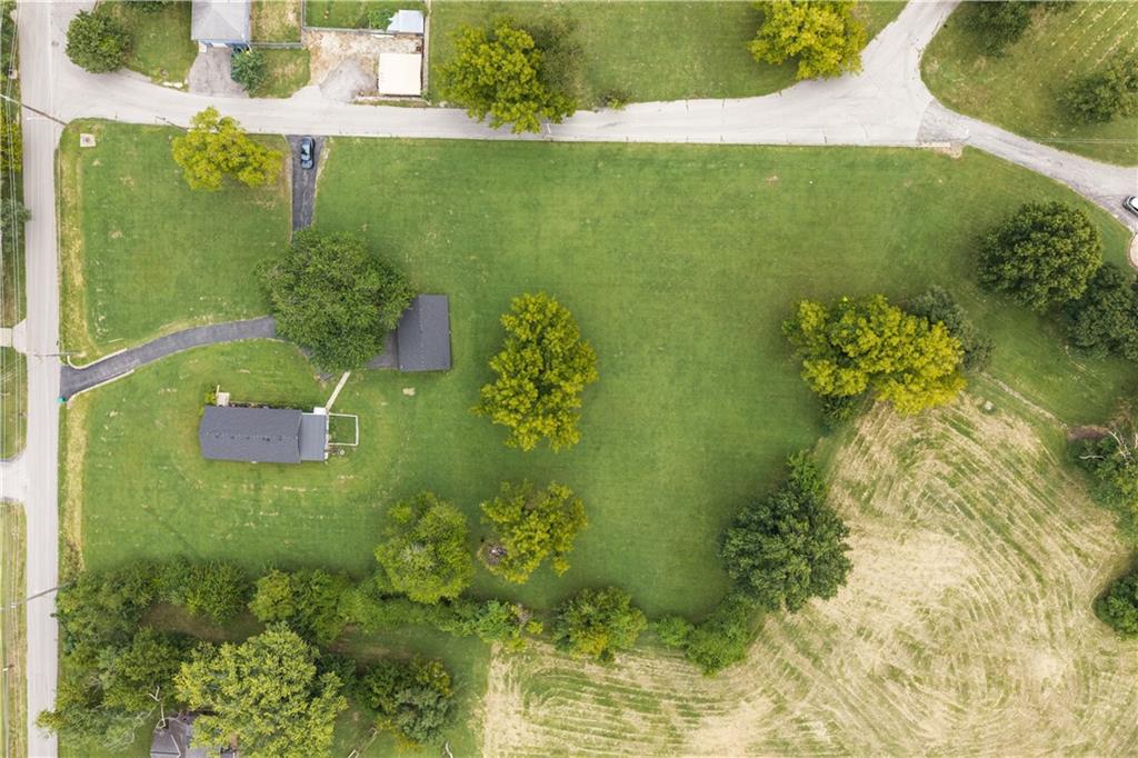 Aerial view of a grassy property with scattered trees, two outbuildings, and a curving driveway.