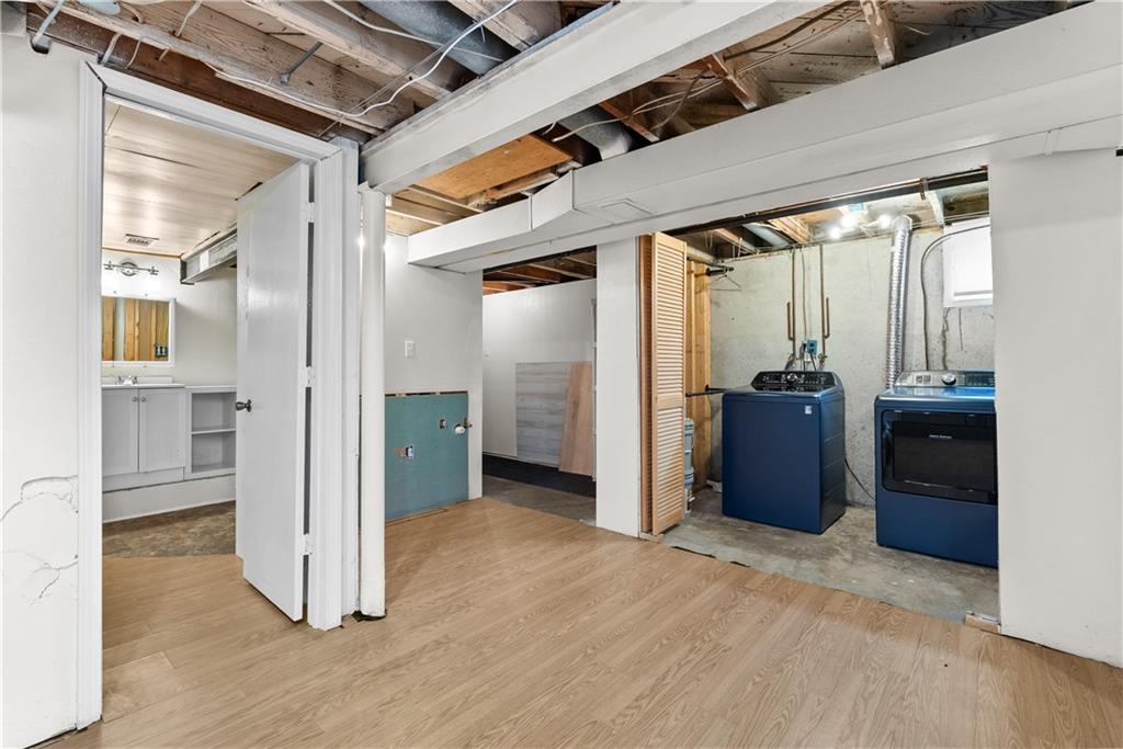 Basement laundry area with blue washer and dryer and exposed ceiling joists.