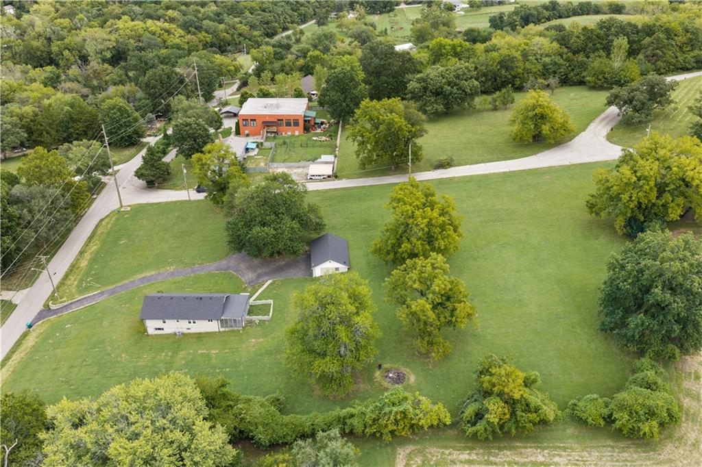 Aerial view of a tree-lined grassy property with two small buildings and a driveway.