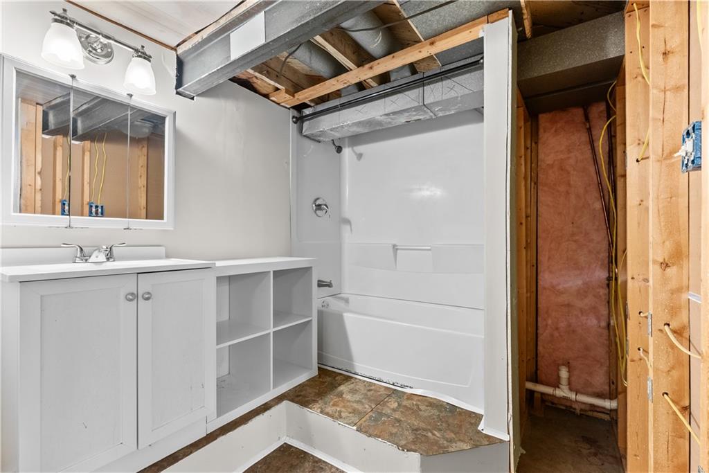 Bathroom with white vanity and tub, exposed ceiling framing, and unfinished adjoining area.