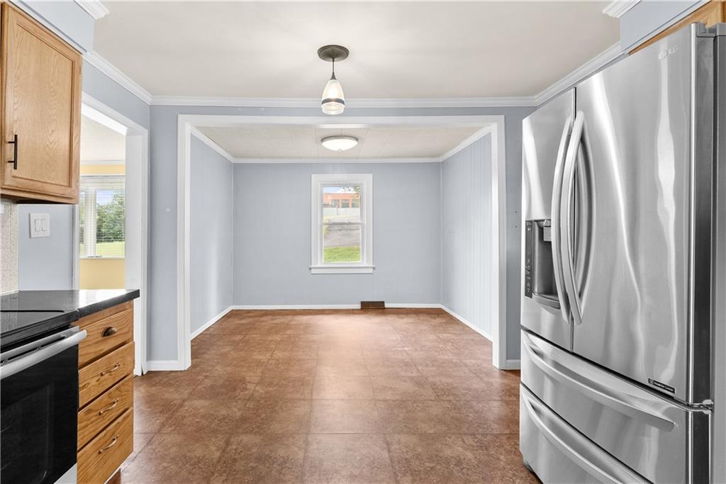 Kitchen opening onto an empty dining area with brown tile flooring and a stainless steel refrigerator.