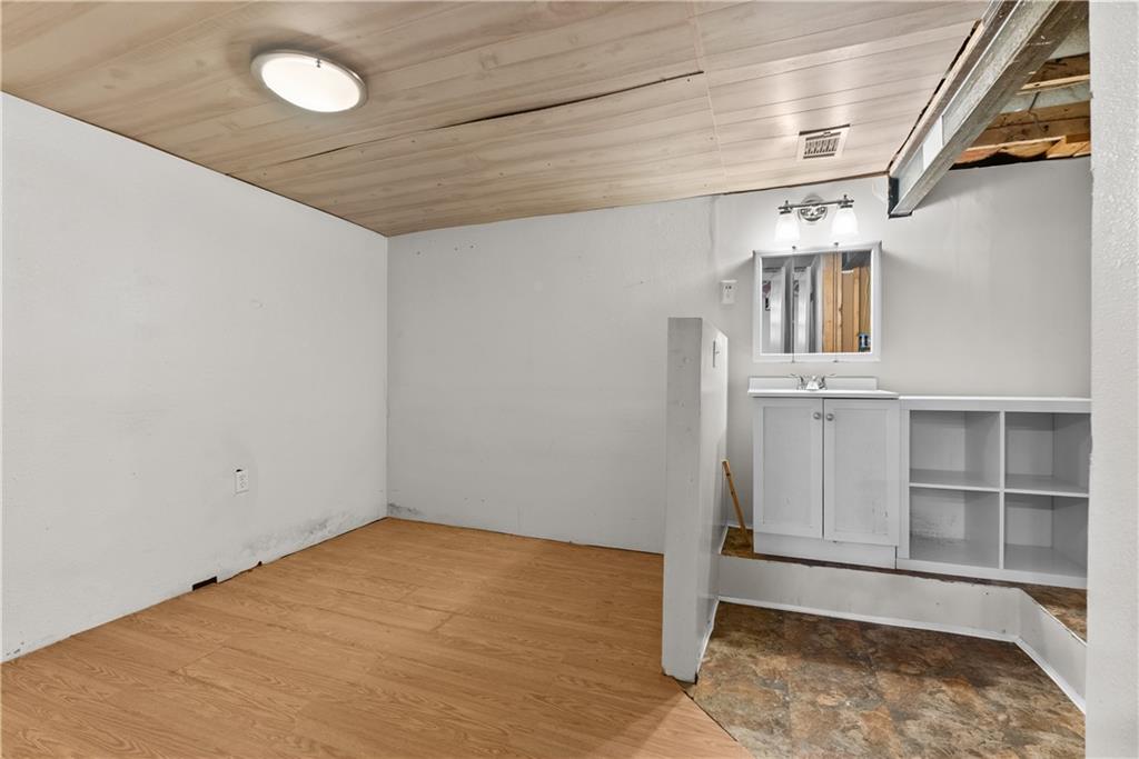 Empty basement room with wood-look flooring, a small sink vanity, and an exposed ceiling section.