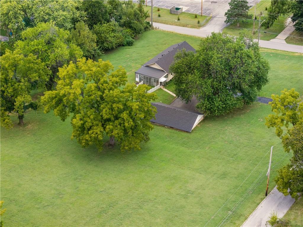 Aerial view of a home amid a broad lawn and mature trees, with a second roofed structure nearby.