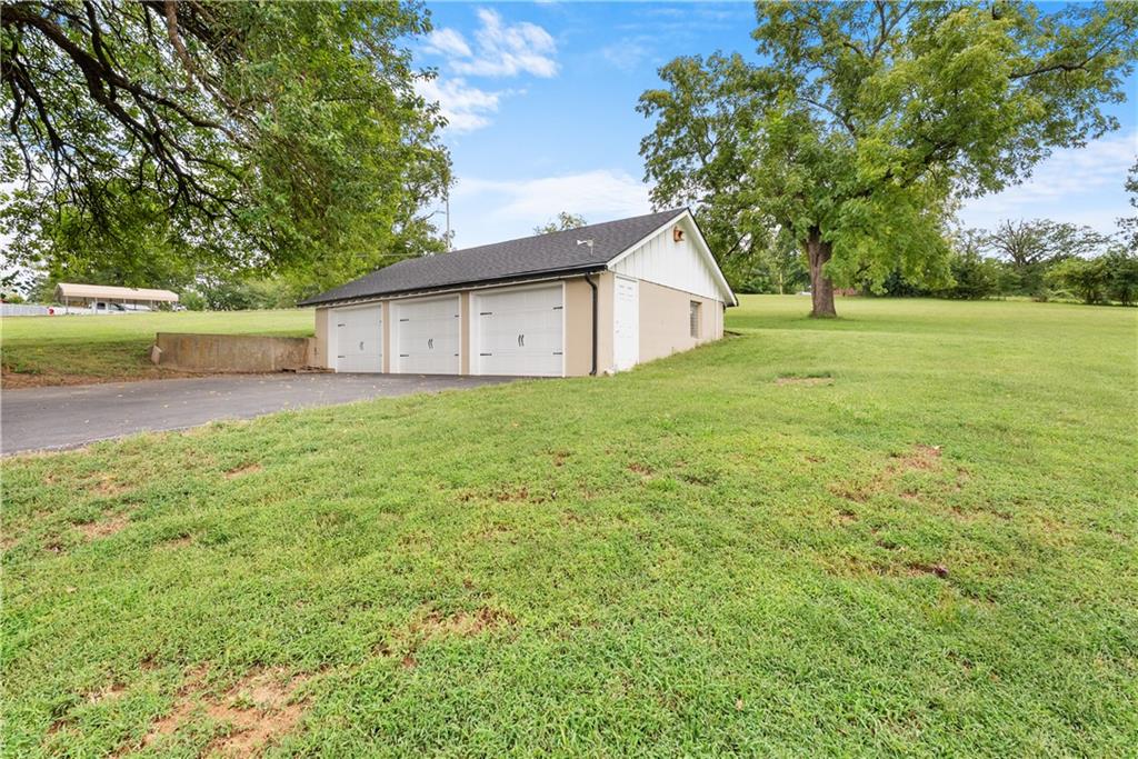 Detached three-door garage beside a paved driveway on a grassy, tree-lined lot.