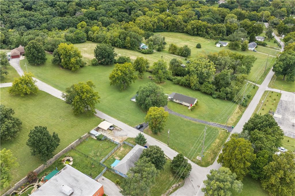 Single-story home on a large grassy lot bordered by mature trees and nearby roads.