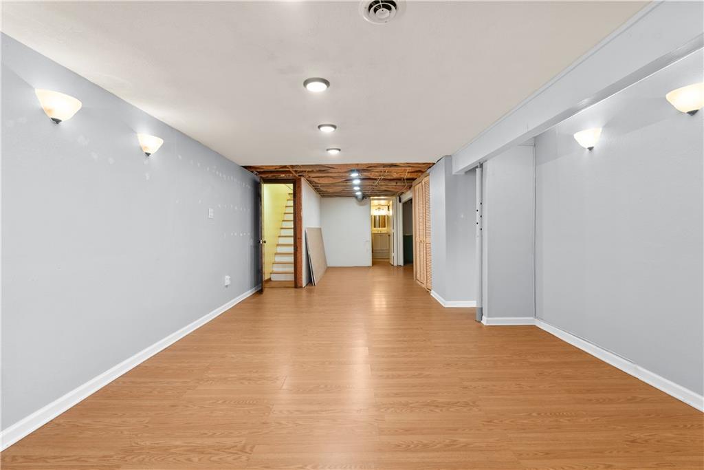 Empty basement room with wood-look flooring, gray walls, and an exposed ceiling near the stairs.