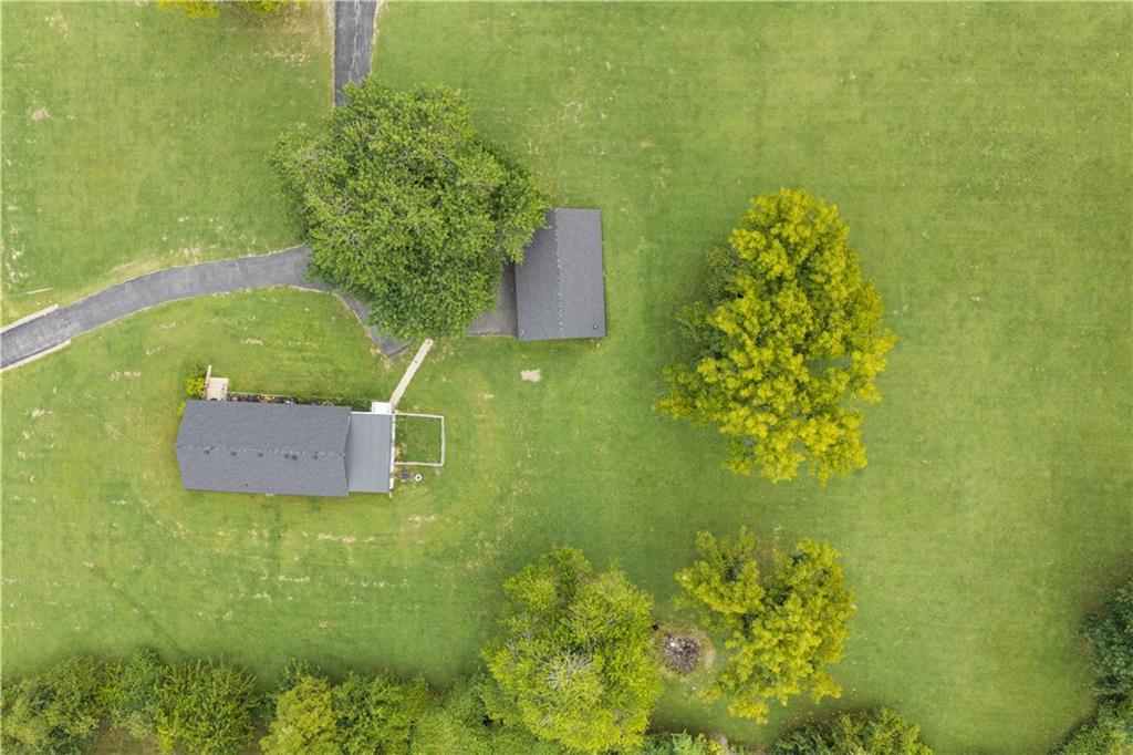 Aerial view of a grassy property with two small buildings, mature trees, and a curved paved path.