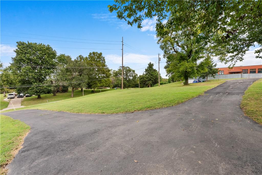 Grassy property grounds with a paved driveway, mature trees, and a building in the background.