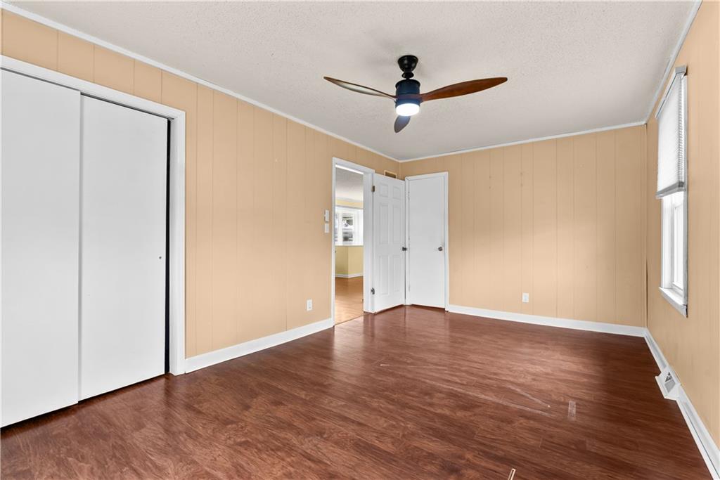 Empty bedroom with tan paneled walls, reddish-brown flooring, a sliding-door closet, and a ceiling fan.