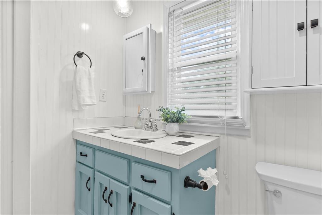 Bathroom with a turquoise vanity, tiled countertop, and window blinds.