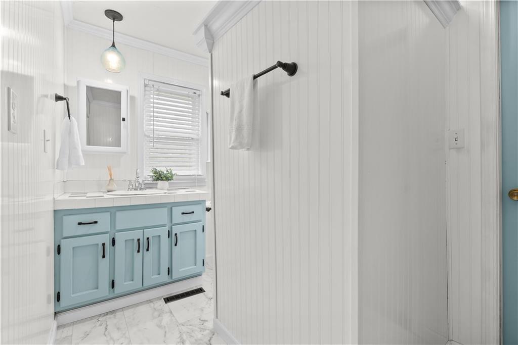 Bathroom with a light blue vanity, window blinds, white beadboard walls, and marble-look tile floor.