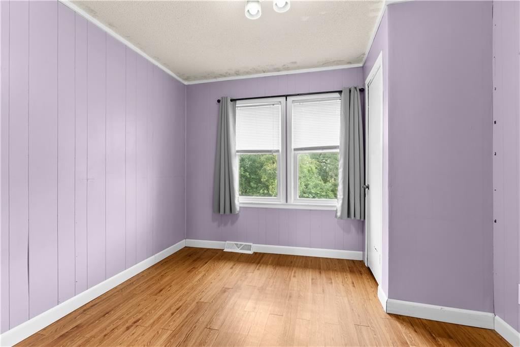 Empty room with lavender paneled walls, wood flooring, and a double window with gray curtains.