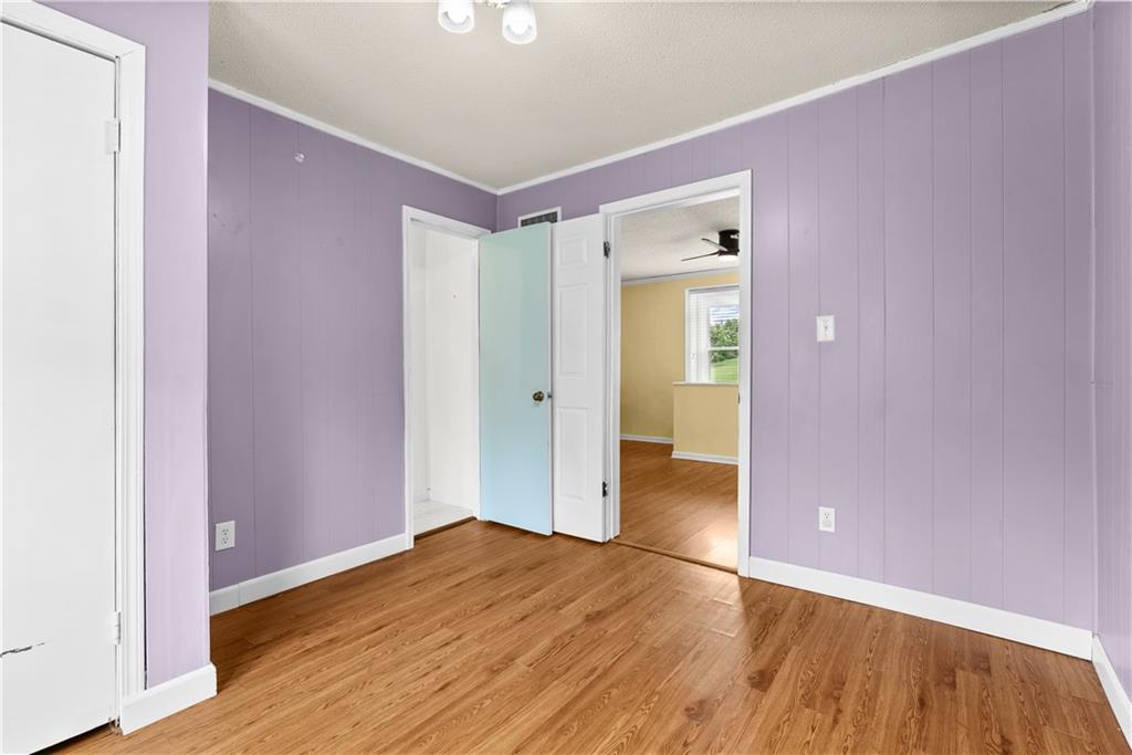 Empty room with lavender paneled walls and wood-look flooring, opening to an adjoining yellow room.