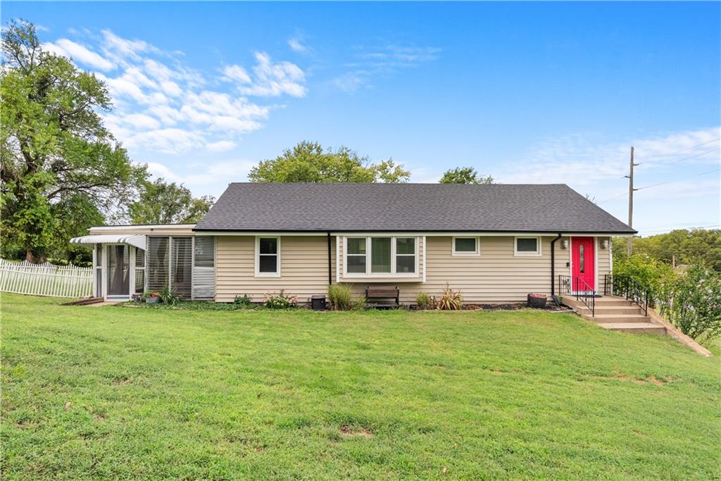 Single-story beige house with a screened porch, broad lawn, and bright red front door.