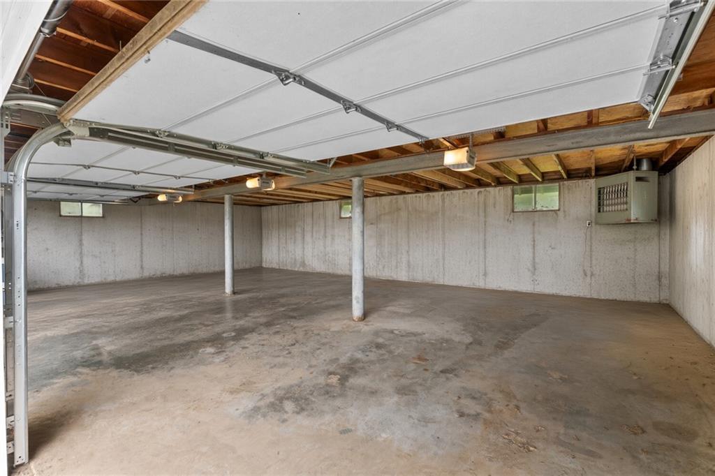 Empty garage with a broad concrete floor, exposed joists, and raised overhead doors.